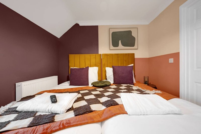 Modern bedroom with dual beds, yellow headboard, patterned bedding and burgundy accent walls