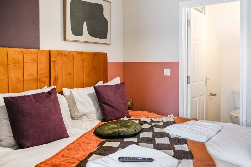 Modern bedroom with orange headboard, purple cushions, patterned bedding and wall art