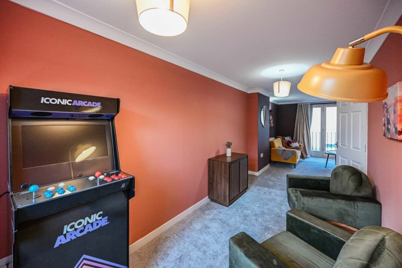 Game room with arcade machine, orange walls, blue carpet, and gray seating