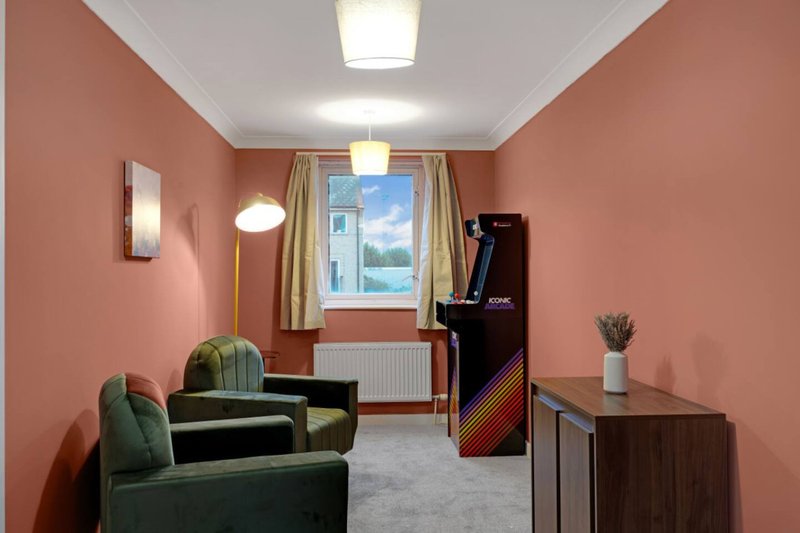 Salmon-pink living room with green armchair, window, wooden furniture and ceiling lights