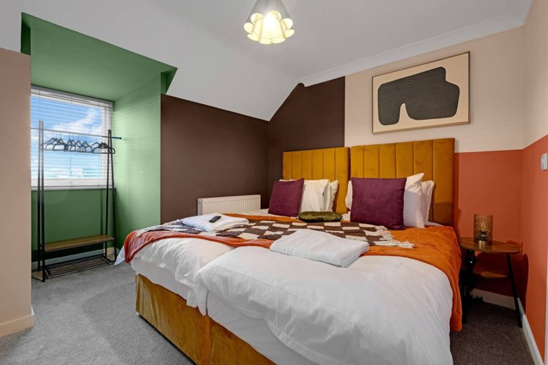 Colorful bedroom with double bed, mustard headboard, purple pillows and orange bedding