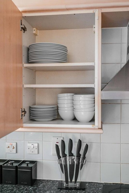 Kitchen cabinet interior with stacked plates, bowls, and knife block on countertop