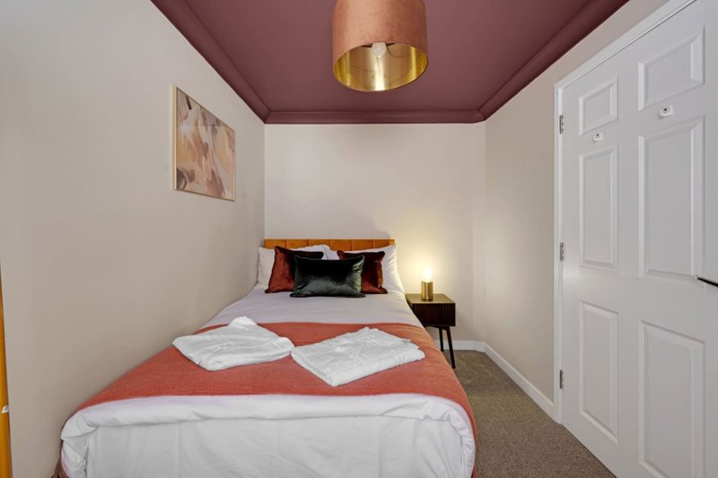 Compact bedroom with single bed, burgundy ceiling, gold pendant light, and white wardrobe