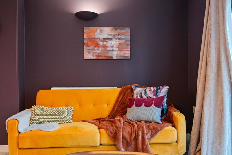 Modern living room with orange velvet sofa, colorful cushions, and abstract wall art