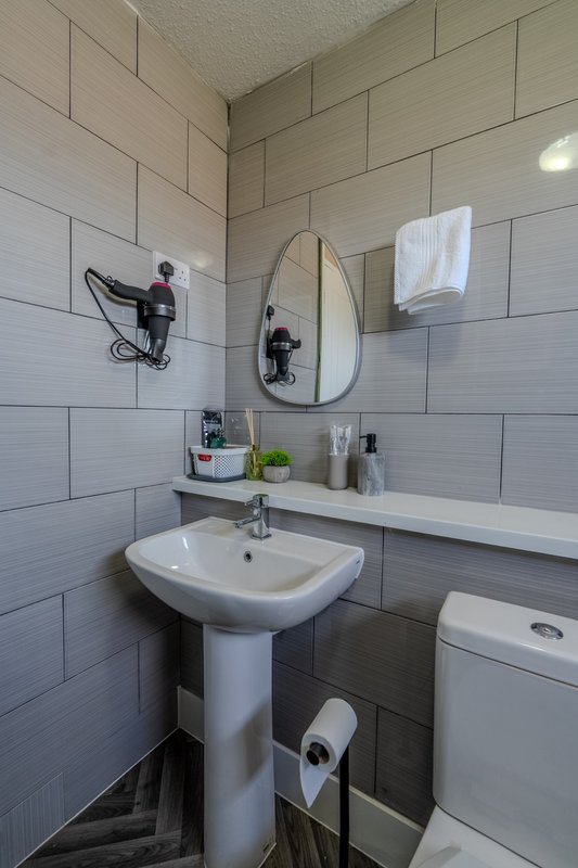 Modern bathroom with pedestal sink, oval mirror, white subway tile walls and toilet