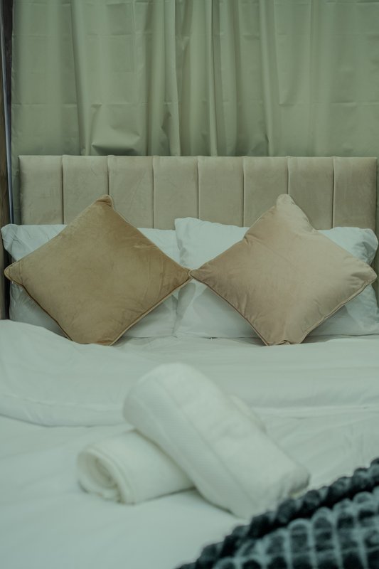 Bedroom with upholstered headboard, beige cushions, white bedding and rolled towels