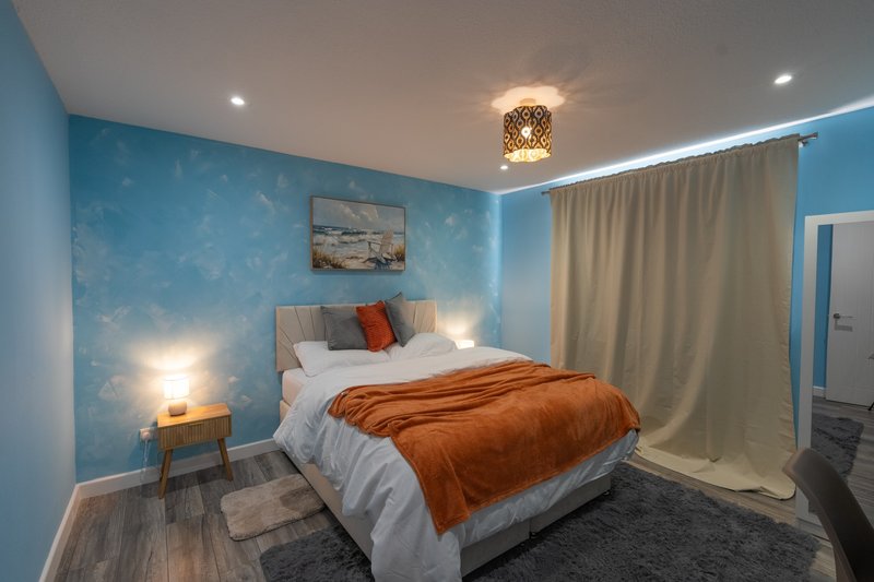 Bright blue bedroom with double bed, orange throw, wooden nightstands and recessed ceiling lights