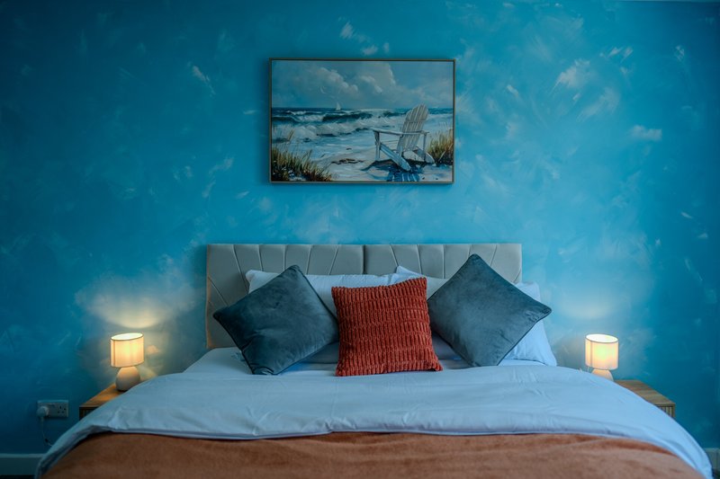 Modern bedroom with blue accent wall, grey upholstered headboard, decorative cushions and bedside lamps