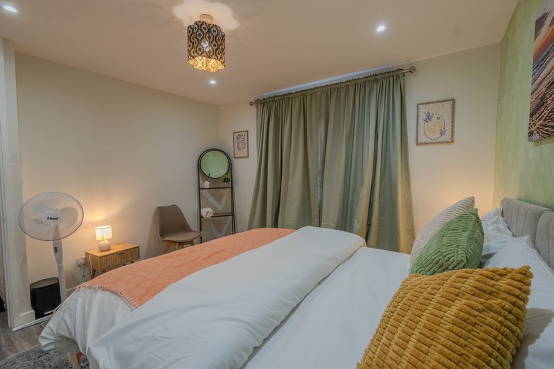 Bright bedroom with double bed, green curtains, decorative pillows and ceiling lamp