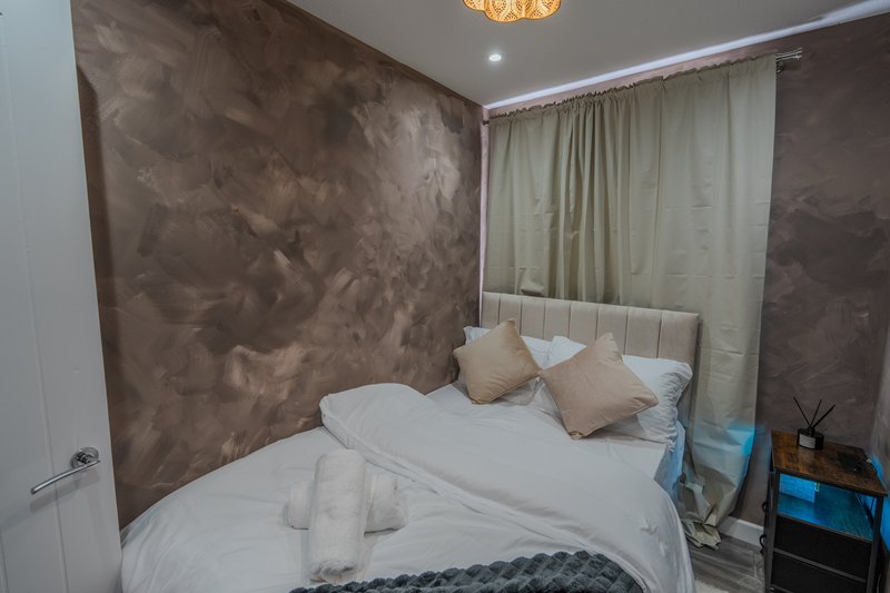 Modern bedroom with double bed, brown accent wall, cream curtains and ceiling light