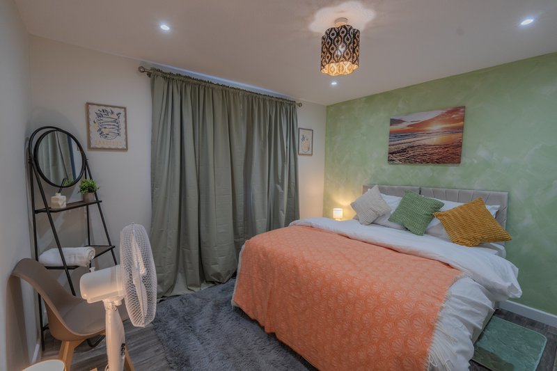 Bedroom with double bed, green feature wall, curtains, desk fan and pendant ceiling light
