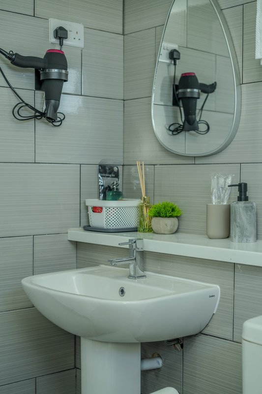 Modern bathroom with wall-mounted sink, mirror, showerhead, and shelf with toiletries
