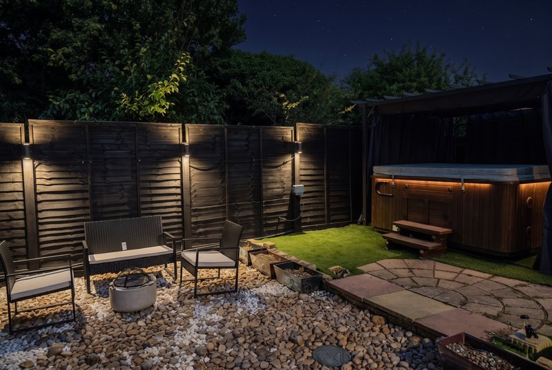 Night-time garden with seating area, fire pit, lighting, hot tub and lawn