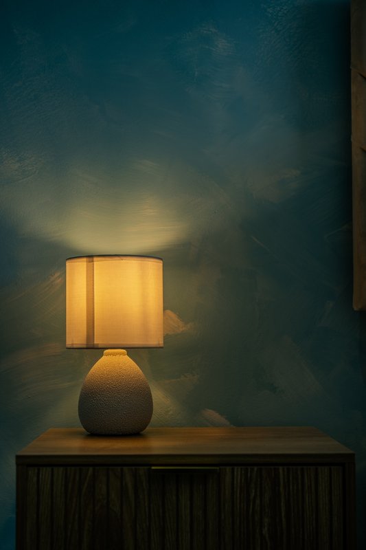 Bedside table lamp with textured base and square shade against teal wall