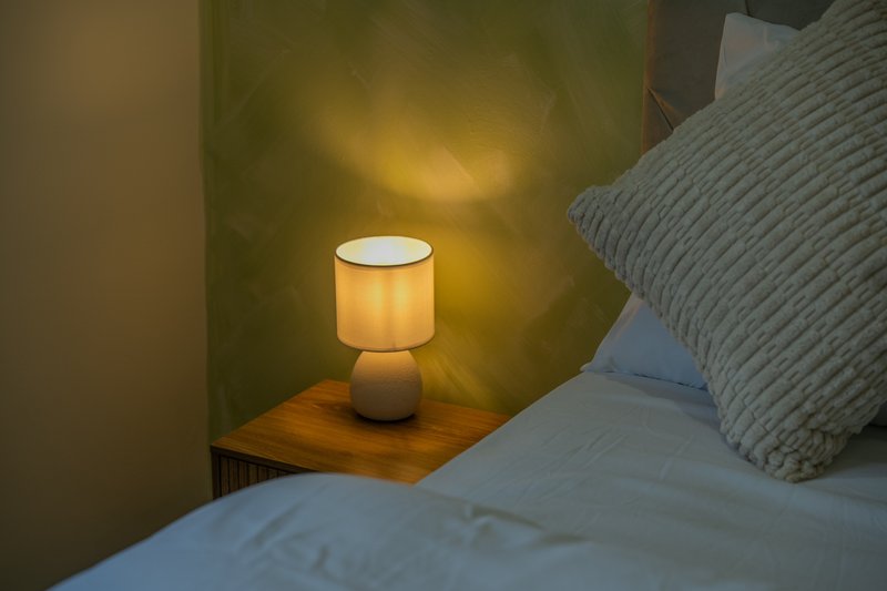 Bedroom bedside table with illuminated lamp and rumpled bedding