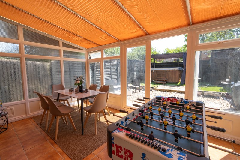 Bright sunroom with dining table, foosball table, and garden views through windows