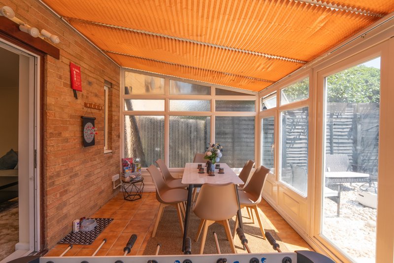 Bright sunroom with wooden floors, dining table, chairs, and large windows overlooking garden