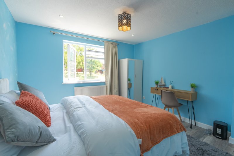 Bright blue bedroom with double bed, orange throw, white pillows and window with garden view