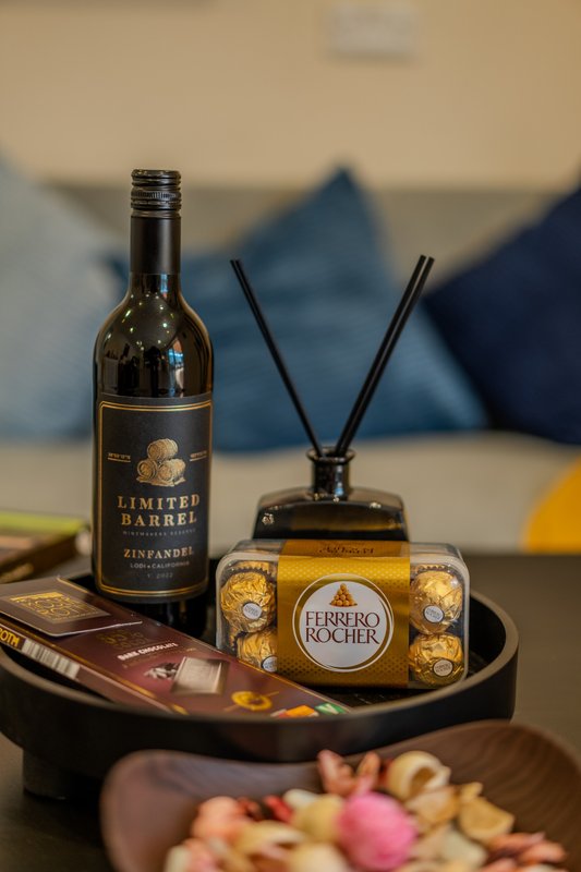 Still life arrangement with wine bottle, reed diffuser, chocolates, and decorative items on table
