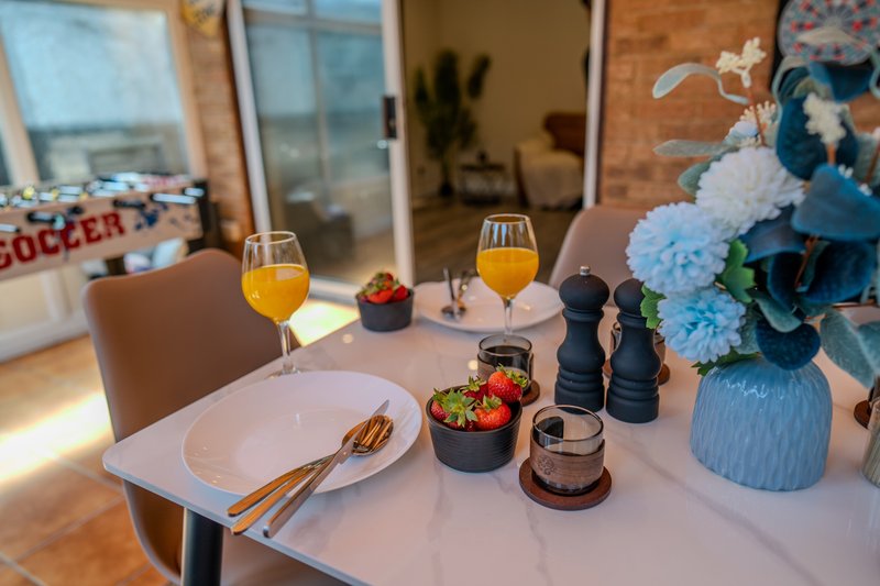 Dining table set with place settings, orange juice, flowers, and decorative items in bright room