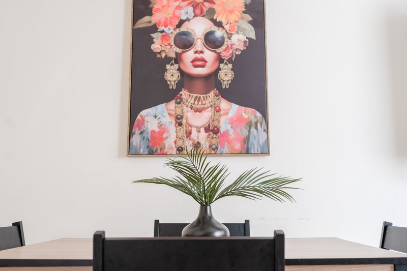 Dining area with black chairs, wooden table, and potted plant under wall art