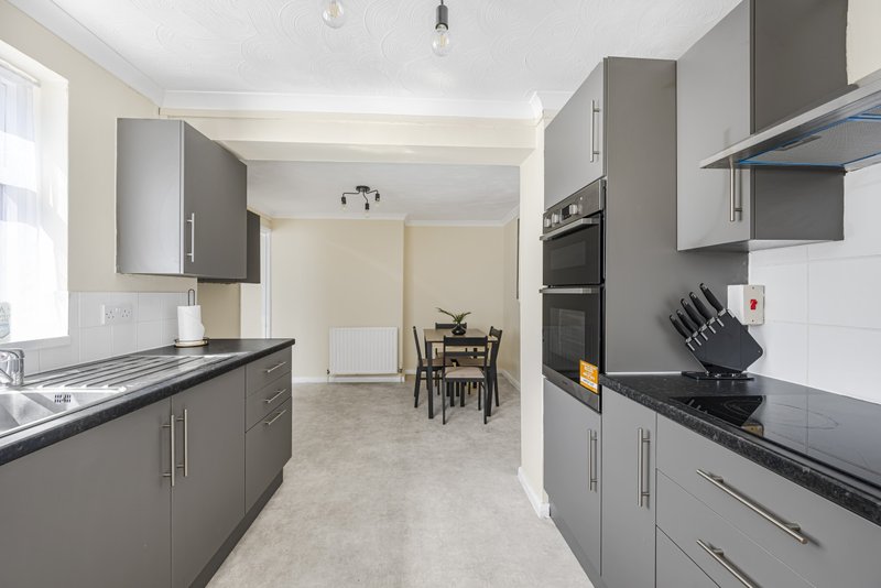 Modern galley kitchen with grey cabinetry, black countertops, and dining area visible beyond