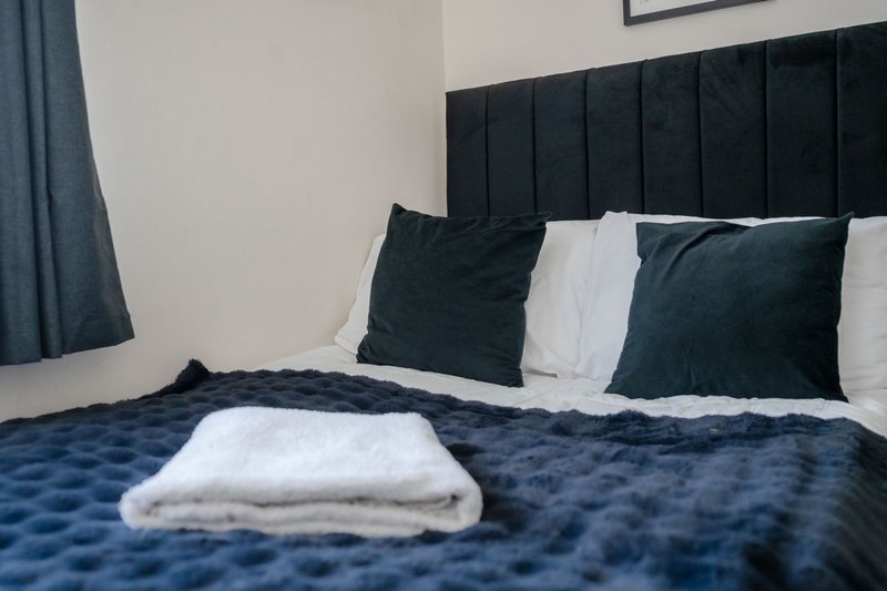 Modern bedroom with black upholstered headboard, dark blue bedding, and white towel