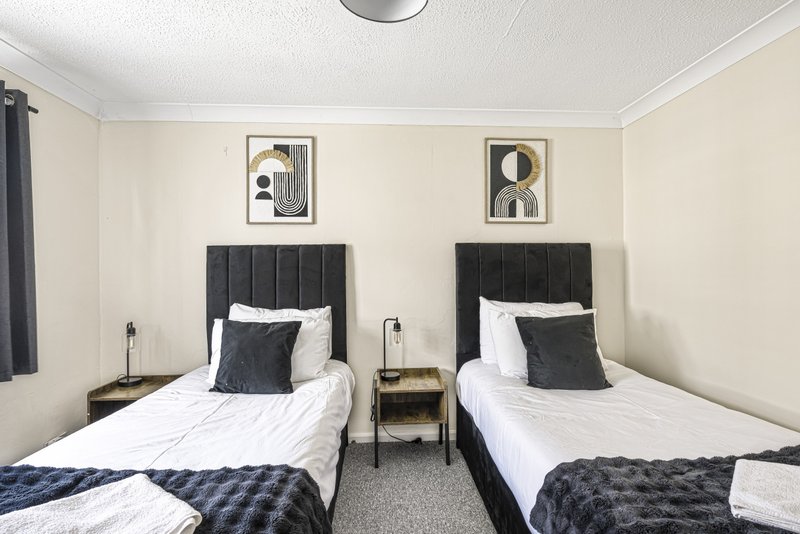 Twin bedroom with two single beds, dark headboards, white bedding, and framed wall art