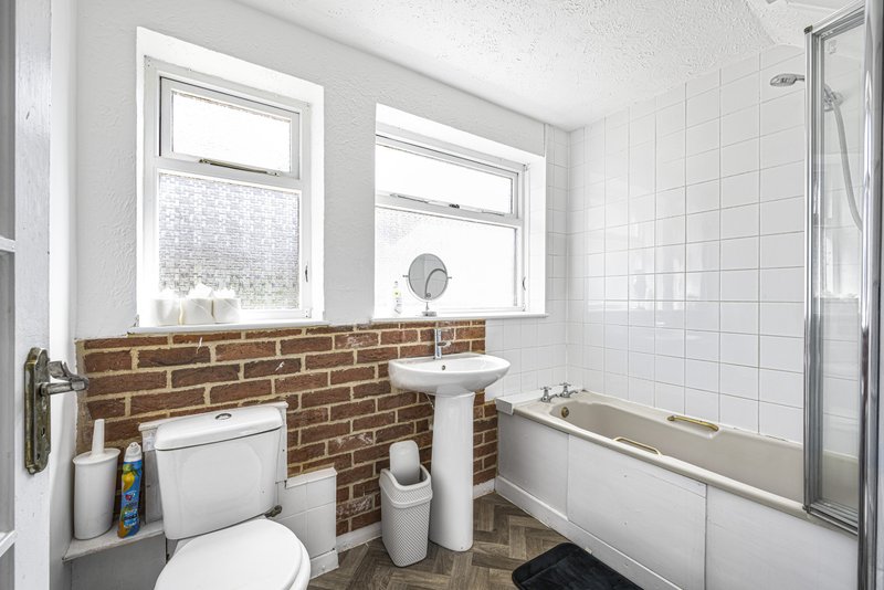 Modern bathroom with white tiles, brick feature wall, toilet, pedestal sink, and bathtub with shower enclosure