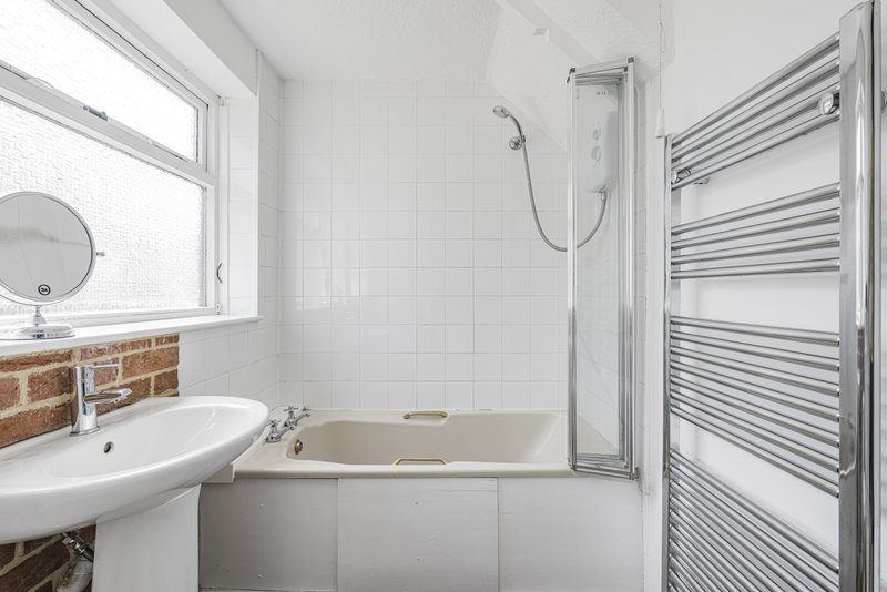 Modern bathroom with white subway tiles, pedestal sink, bathtub with shower screen, and heated towel rail