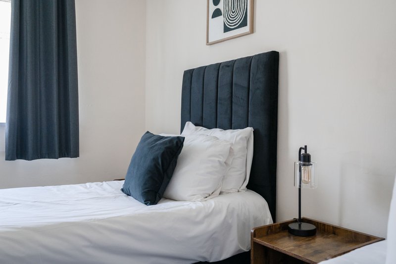Modern bedroom with dark upholstered headboard, white bedding, blue cushion and curtains