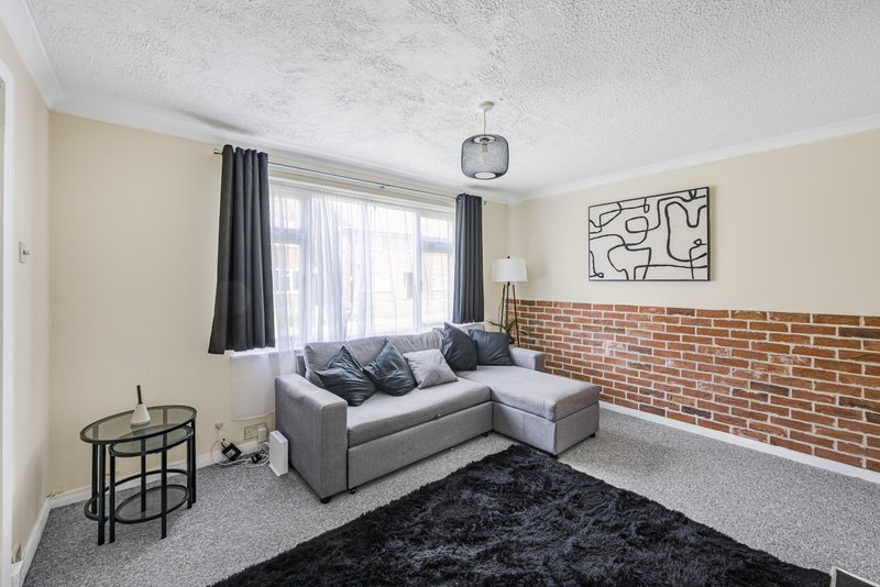 Modern living room with grey corner sofa, exposed brick wall, large windows and abstract wall art
