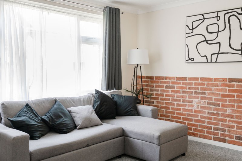 Modern living room with grey corner sofa, decorative pillows, exposed brick wall and abstract artwork
