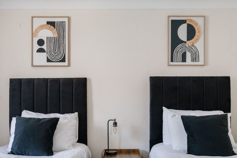 Twin bedroom with black upholstered headboards, white bedding, dark cushions, and abstract wall art