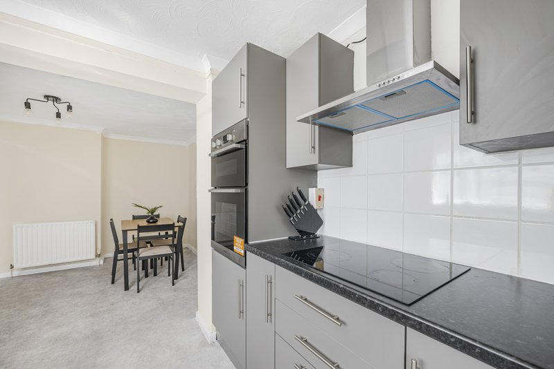 Modern kitchen with white cabinets, black countertop, and dining area visible in background