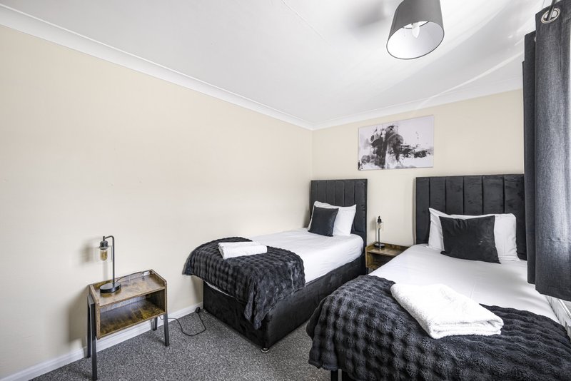 Twin bedroom with black upholstered headboards, white bedding, cream walls and ceiling light