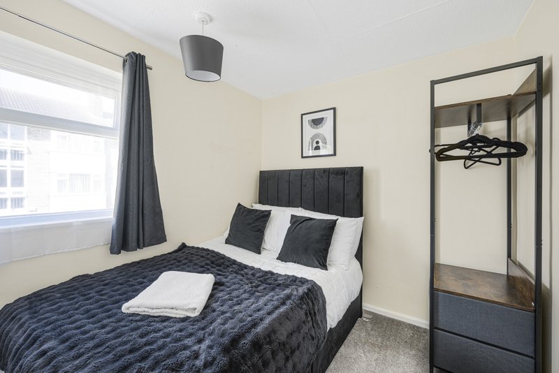Modern bedroom with double bed, black quilted bedding, white pillows and grey curtains