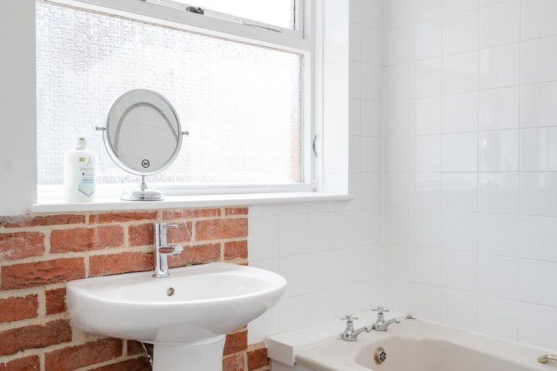 Modern bathroom with pedestal sink, round mirror, red brick accent wall and white tile surround
