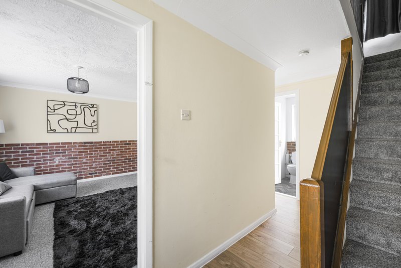 Hallway with wooden banister, cream walls, and view into living room with brick fireplace
