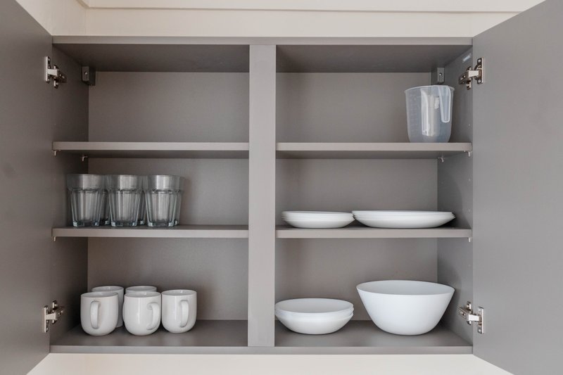 Open kitchen cabinet with white dishes, bowls, glasses and storage containers on shelves