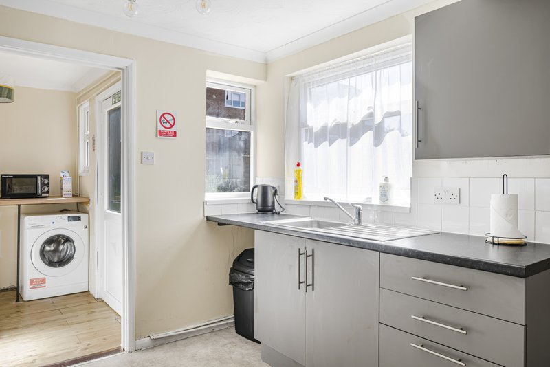 Modern kitchen with gray cabinetry, black countertop, sink, washing machine and window