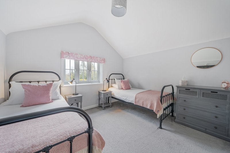 Bright bedroom with two single beds, grey dresser, round mirror and window with pink accents