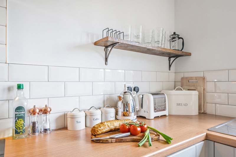 Modern kitchen counter with white subway tile backsplash, wooden shelf, and fresh produce