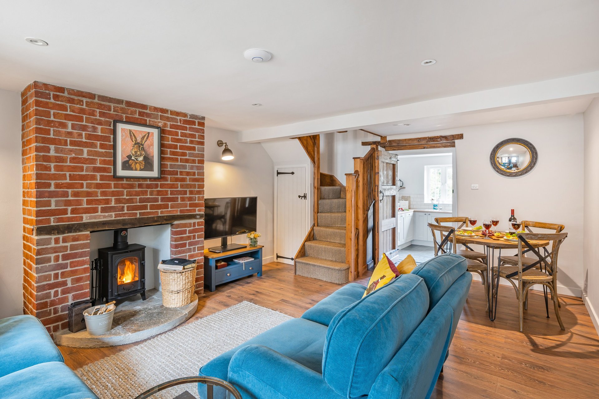 Open-plan living room with blue sofa, brick fireplace with wood-burning stove, wooden stairs, and dining area