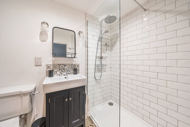 Modern bathroom with white subway tile shower, black vanity unit, mirror and wall sconces
