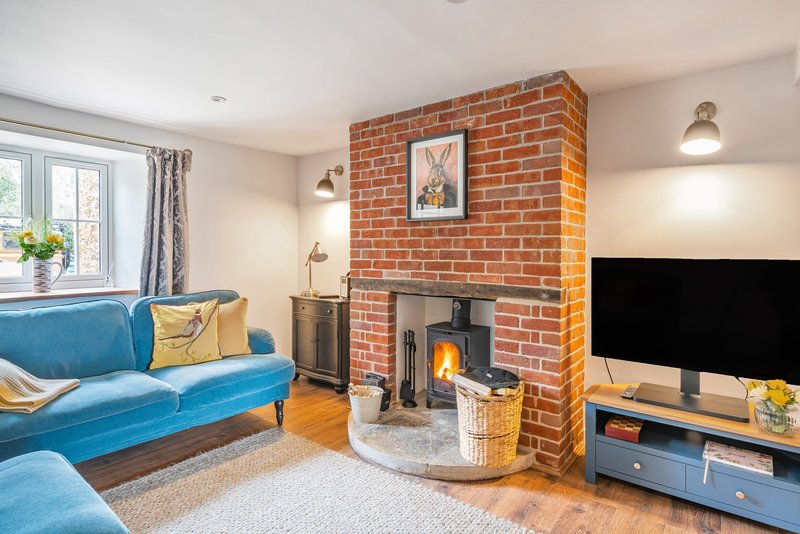 Living room with blue sofa, brick fireplace with wood stove, TV stand and window