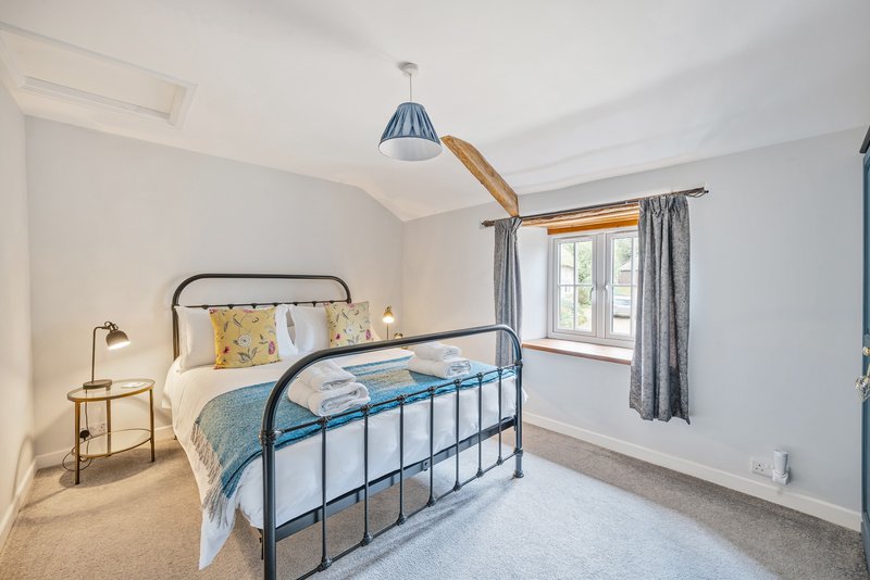 Bright bedroom with metal frame bed, pendant light, wooden beams and grey curtains