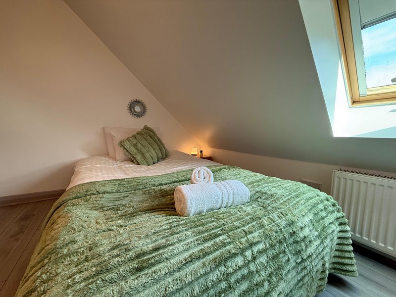Attic bedroom with double bed, green bedding, pillows, skylight window and radiator