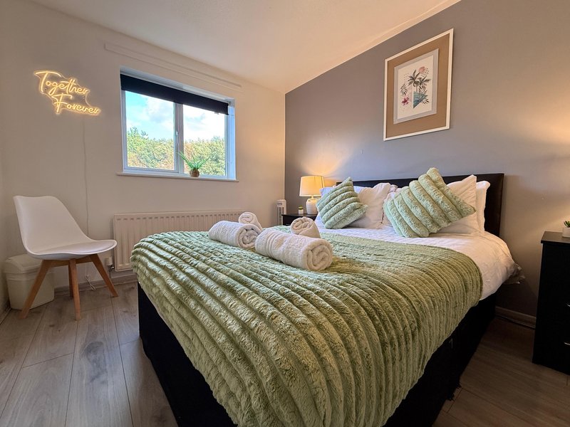 Bedroom with double bed, green bedding, white chair, window and wall art