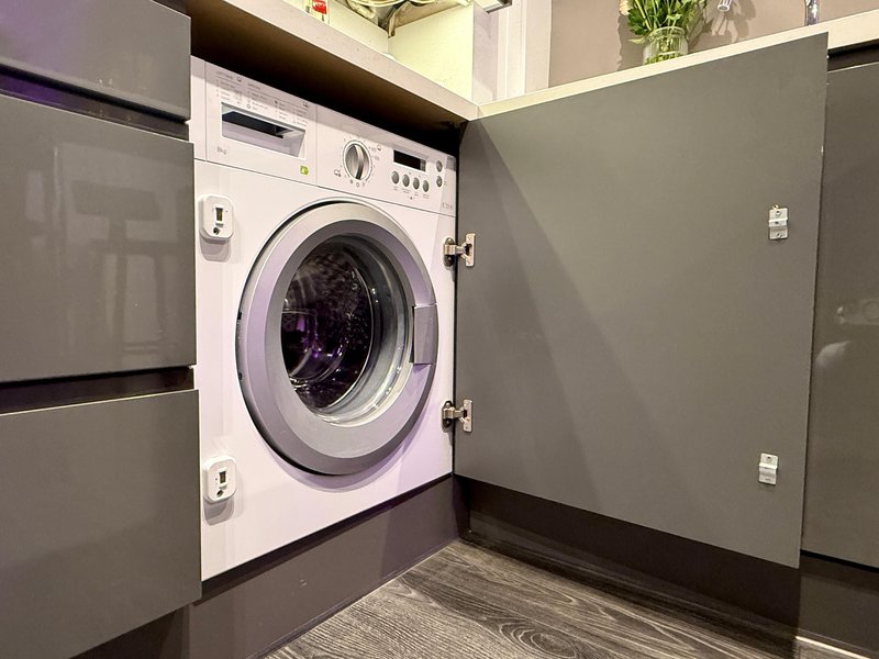 Built-in washing machine in fitted kitchen with grey cabinetry and dark flooring